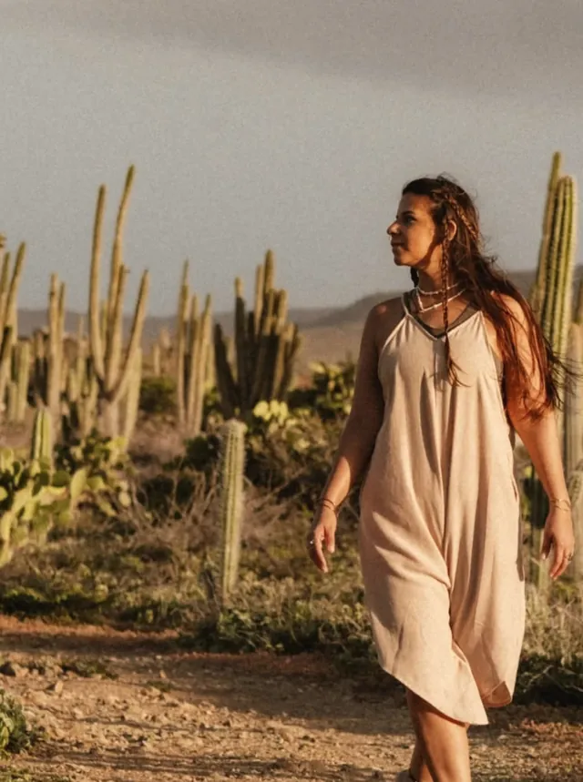 Janine walking barefoot along a dirt path between tall cacti in the Aruban countryside