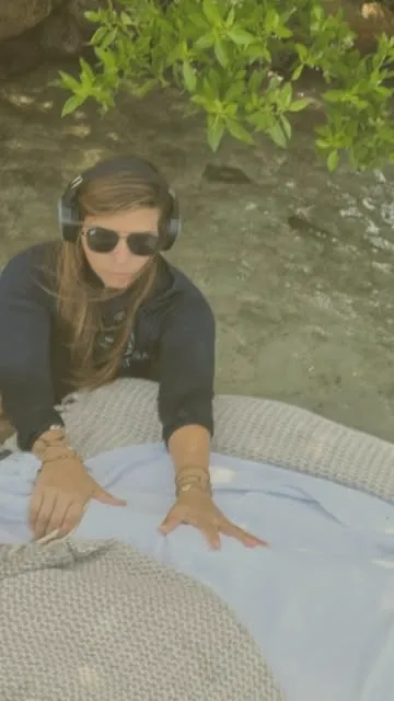 Janine wearing headphones at the water's edge, preparing a float for a session