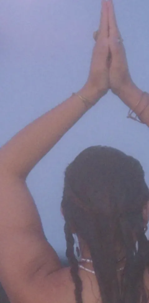 Hands joined above the head in a yoga pose, seen from behind against a blue dusk sky