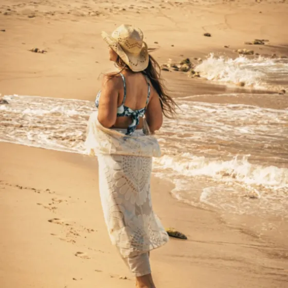 A woman in a straw hat walking along the shoreline as small waves reach the sand