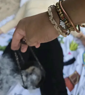 A hand with bracelets holding a smoking censer on a chain